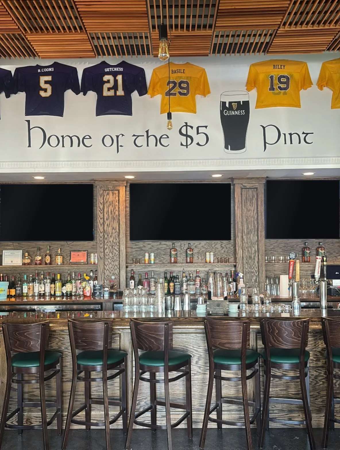 The bar at Angus Irish Pub: a row of stools, the back bar and three televisions, under a wall lettered Home of the $5 Pint