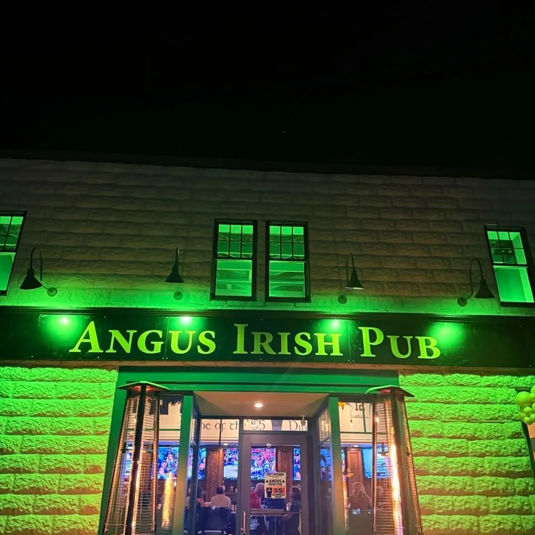The front of Angus Irish Pub at night, lit green, with its name over the door